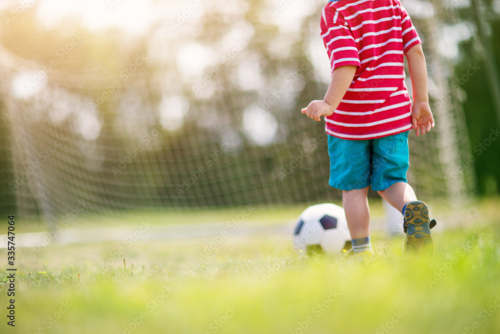 Little boy playting football on the field with gates Little boy playting football on the field with gates