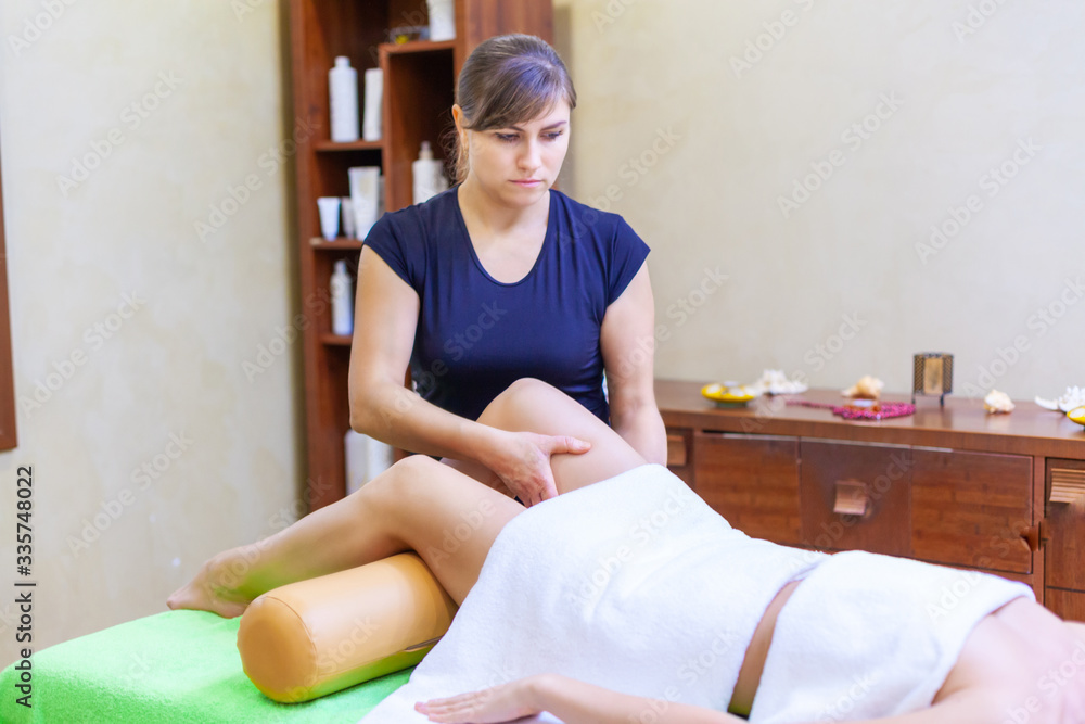 Front view of professional massage therapist giving massage on woman legs in the spa salon Front view of professional massage therapist giving massage on woman legs in the spa salon