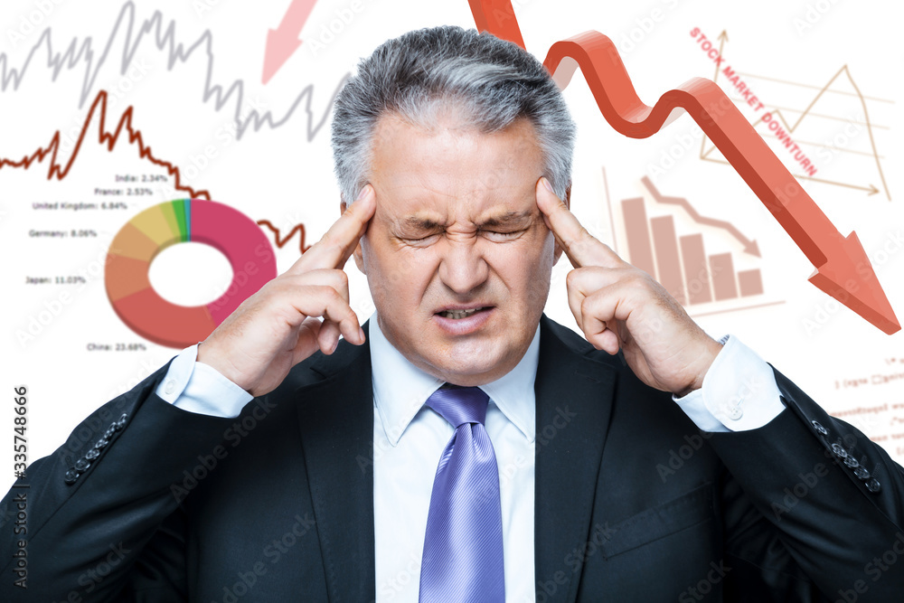 Coronavirus Stock Market Crash. Economic impact of COVID-19. Stressed mature businessman feeling depressed while standing against background with financial graphs and charts. Global Coronavirus crisis Coronavirus Stock Market Crash. Economic impact of COVID-19. Stressed mature businessman feeling depressed while standing against background with financial graphs and charts. Global Coronavirus crisis