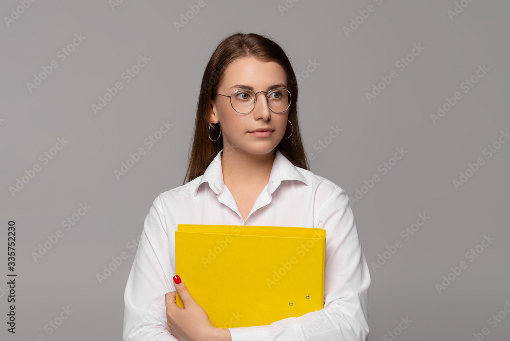 smiling young businesswoman in white shirt with yellow folder isolated on grey smiling young businesswoman in white shirt with yellow folder isolated on grey