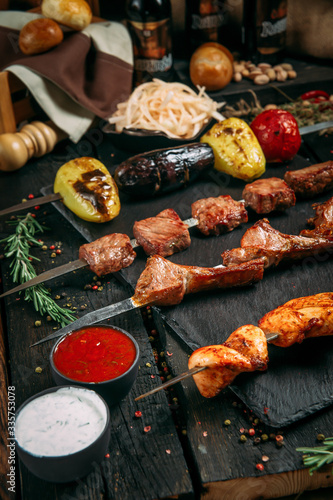 appetizing assorted set kebab sticks with red sauce and pickled onion on a black board on a dark wooden background, side view, vertical