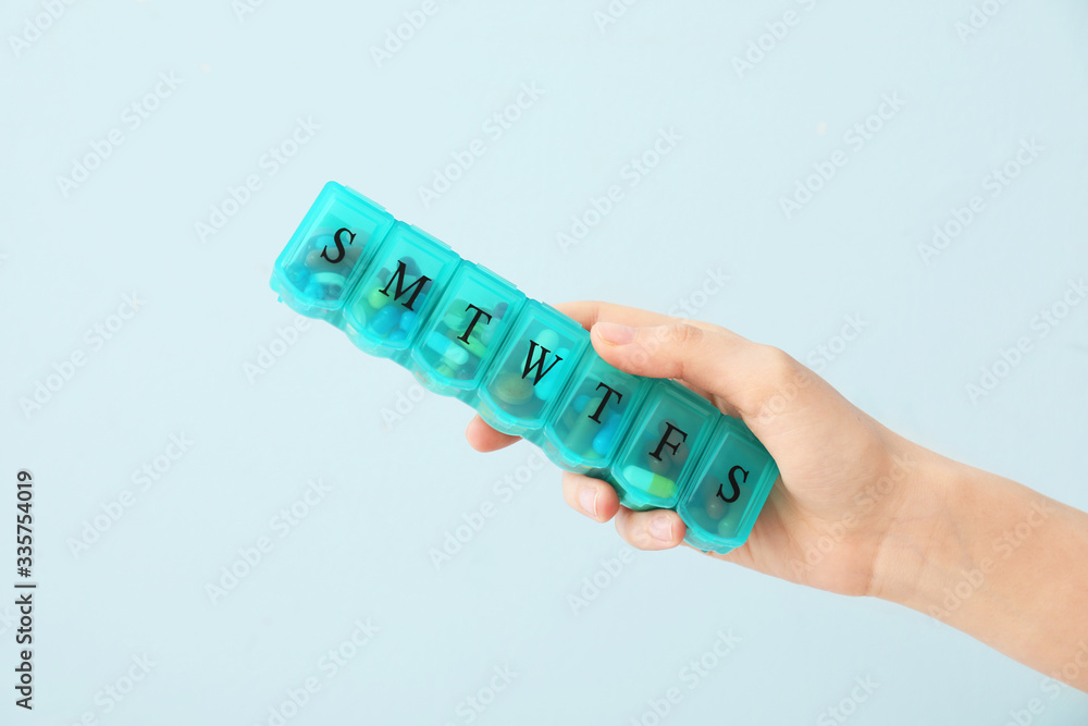 Obraz premium Female hand holding box with pills on color background