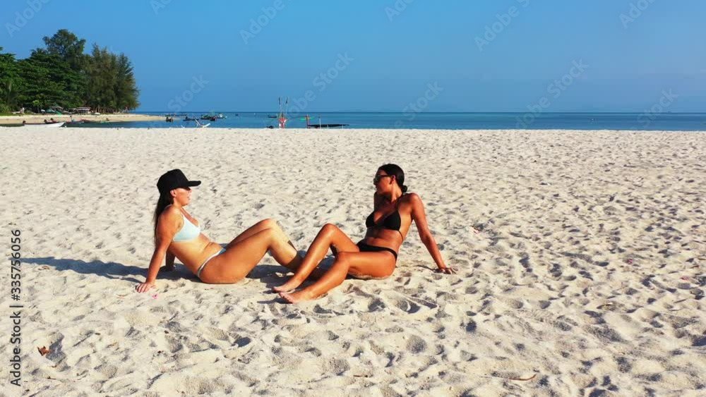 Attractive young ladies in bikini sunbathe on white sandy beach near holiday resort on tropical island of Indonesia Attractive young ladies in bikini sunbathe on white sandy beach near holiday resort on tropical island of Indonesia