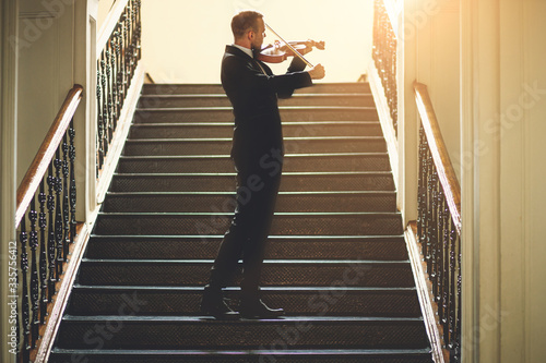 Fotografia young caucasian male violinist practice music performance on the stairs in the hall, handsome guy musician love his job in theatre
