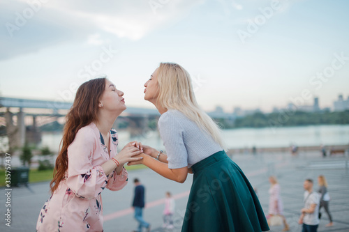 Two cute girls sending air kisses to eacn othes. Outdoor photo of young women. photo