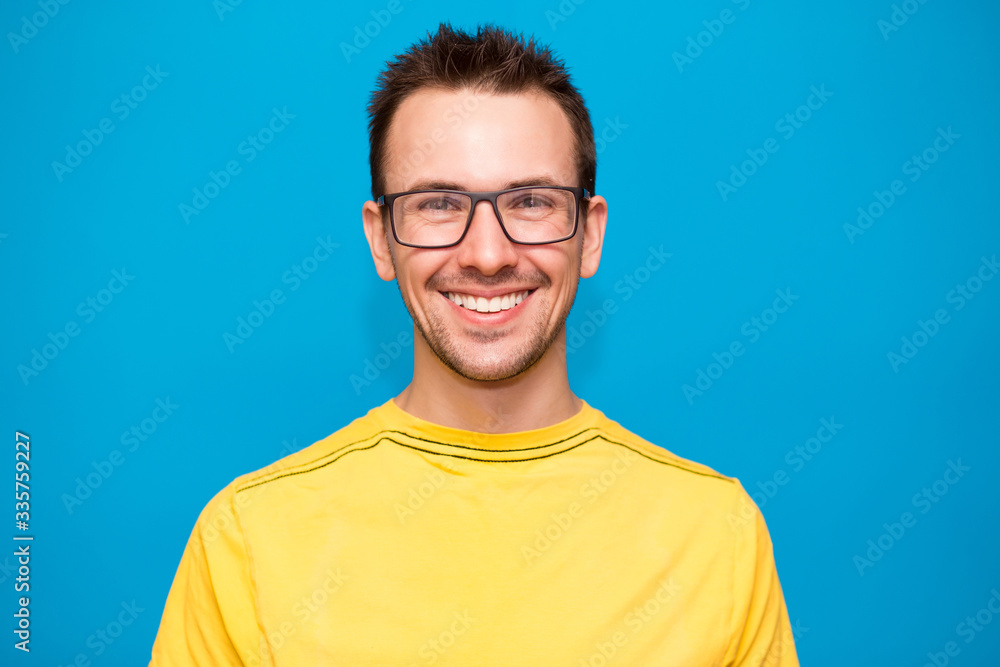 Portrait of handsome young man in glasses and yellow t-shirt isolated on blue background Portrait of handsome young man in glasses and yellow t-shirt isolated on blue background