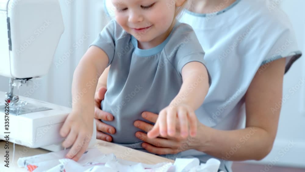 Concept during self-isolation and quarantine. A woman with a small child sews a protective mask. Concept during self-isolation and quarantine. A woman with a small child sews a protective mask.