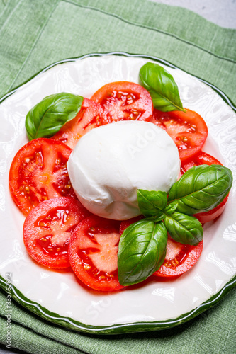 Tasty italian fresh salad with white soft cheese mozzarella ball, red tomatoes and fresh green basil