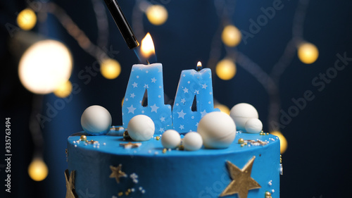 Birthday cake number 44 stars sky and moon concept, blue candle is fire by lighter. Copy space on right side of screen. Close-up