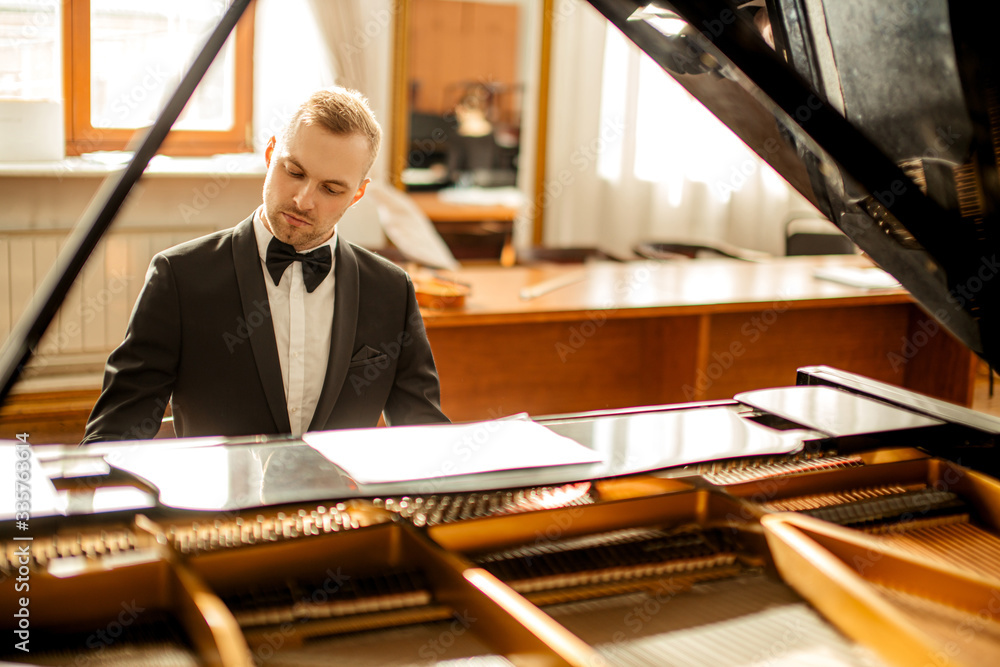 Fototapeta premium young handsome caucasian man in formal elegant suit gracefully play piano. professional pianist perform classic music