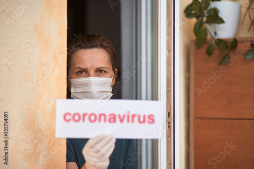 Woman in medical mask holding card with coronavirus lettering. Covid-19.