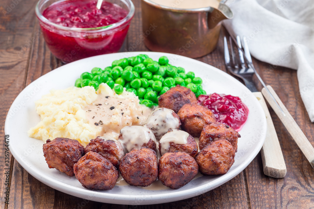 Traditional swedish meatballs served with mashed potato, green peas, cream sauce and cranberry jam, on plate, horizontal Traditional swedish meatballs served with mashed potato, green peas, cream sauce and cranberry jam, on plate, horizontal