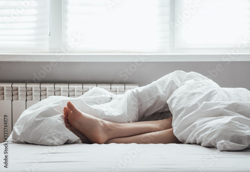 Rest at home. Female legs. Woman lies on the bed under a white blanket.
