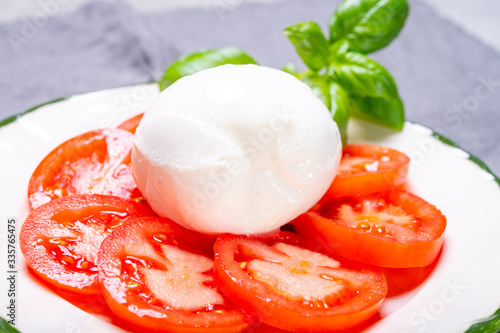 Tasty italian fresh salad with white soft cheese mozzarella ball, red tomatoes and fresh green basil