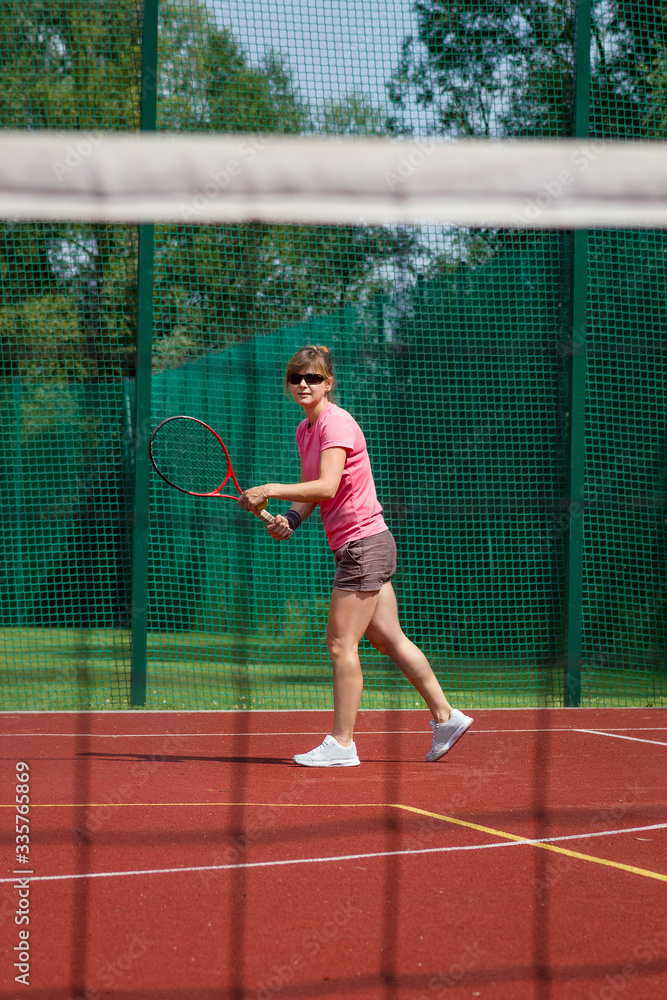 Female tennis player preparing to serve ball. View through net.