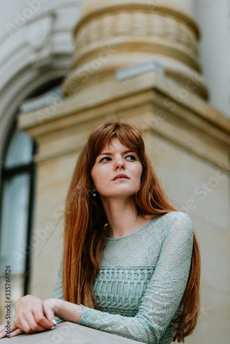 Stylish urban young redhair woman in a fashionable green dress posing in the street. European modern cute model girl enjoys a walk in the city. Spring fashion.