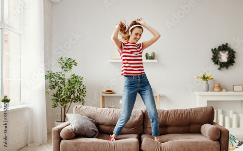 Happy woman listening to music and dancing on couch at home.