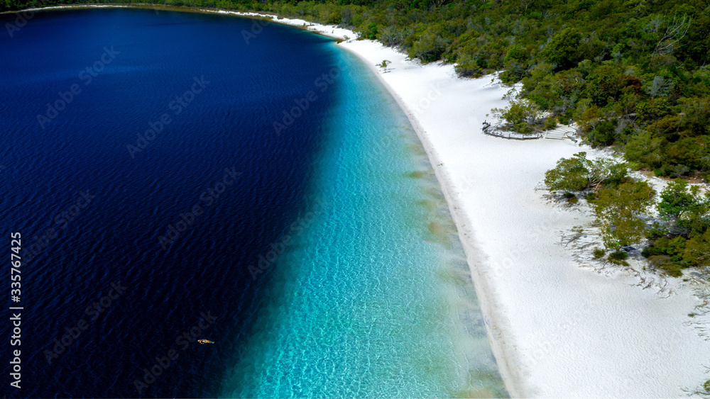 Aerial view of woman swimming in the transparent turquoise Lake Mckenzie in Fraser Island, Australia. Summer seascape with girl, beautiful waves, colorful water at sunset. 
