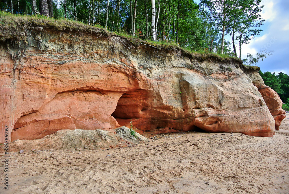 Obraz premium Veczemju klintis, a group of sand cliffs on the Vidzeme coast, red, orange and yellow formations, a sandy beach on the seashore, trees on a hilltop, a beach in Latvia on the shore of the Gulf of Riga.