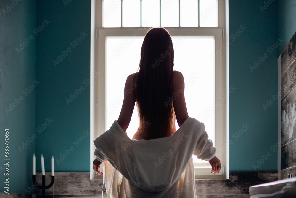 Back view of a woman body entering in the shower with a white ro Back view of a woman body entering in the shower with a white ro