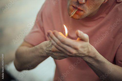 close-up photo of young caucasian guy take drugs at home alone. he lights cannabis weed cigarette. man leads unhealthy lifestyle, he enjoy smoking marijuana, ganja, cannabis. drugs treatment