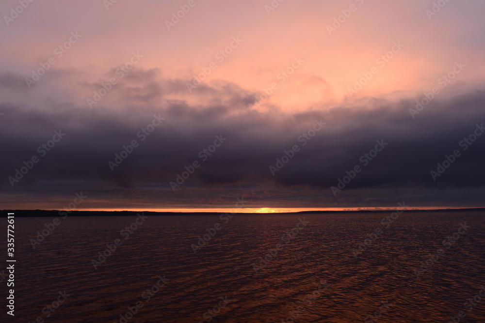 Thunderstorm cloud in sunlight on sunset in the bright ominous sky on the horizon over water