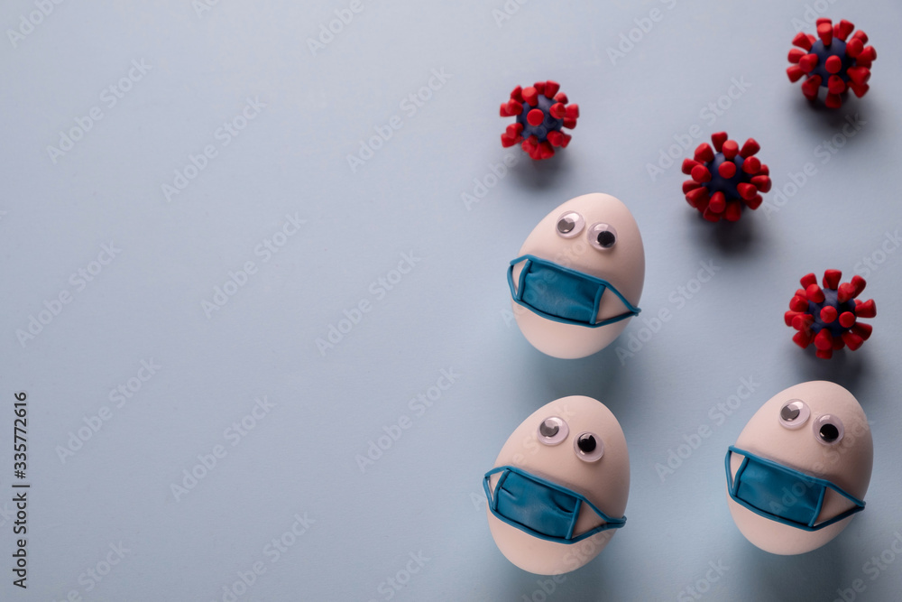 Obraz premium Eggs wearing medical mask for stop coronavirus and models of covid-19 virus on blue background. Epidemic coronavirus COVID-19 concept. Place fo text