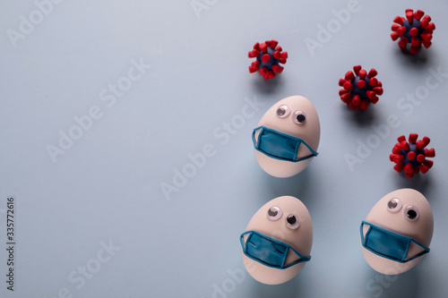 Eggs wearing medical mask for stop coronavirus and models of covid-19 virus on blue background. Epidemic coronavirus COVID-19 concept. Place fo text