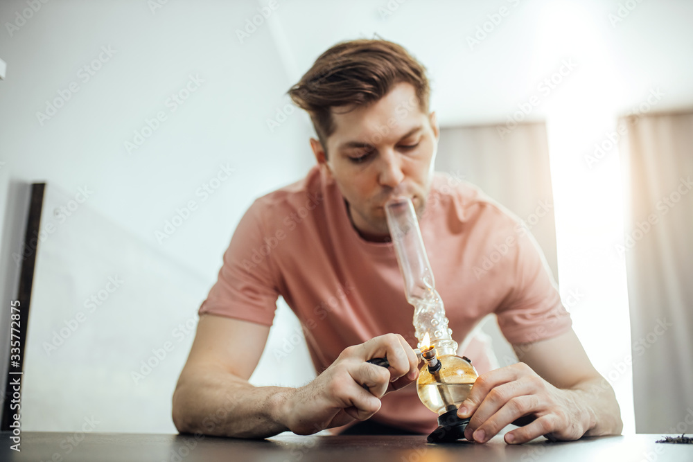 young caucasian man heats bong with marijuana, ganja. young man suffer from  drug addiction, sit at home and enjoy using drugs. tobacco, addiction,  smoking Stock Photo | Adobe Stock