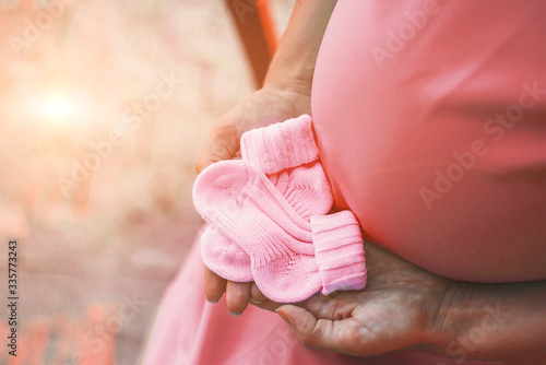belly of a pregnant woman in a pink dress and pink socks for a newborn, place for text 