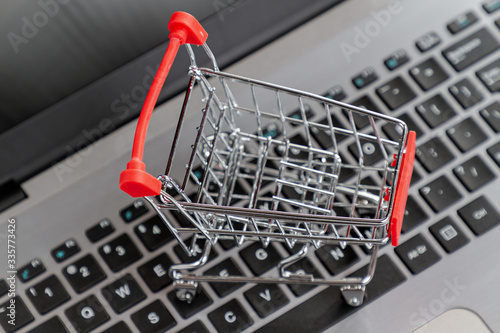 Laptop keyboard with a toy shopping cart standing on it. Close up. Top view. Concept of online shopping and modern technologies