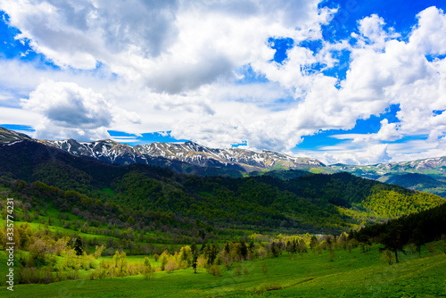 Beautiful mountain panorama with lush greens, blue skies, and puffy clouds © Jim