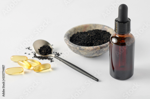 Obraz na płótnie Glass bottle and pills of black cumin seeds essential oil. Nigella Sativa in spoon and bowl on white background w salonie