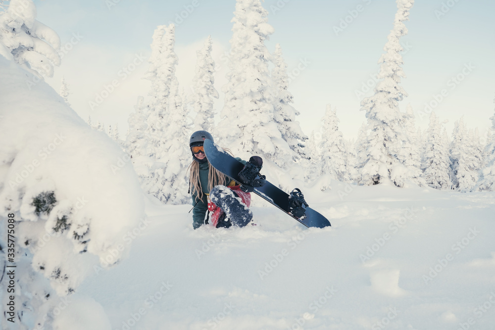 Female snowboarder wearing long dreadlocks and ratsa hoody in white winter forest walking in snow powder