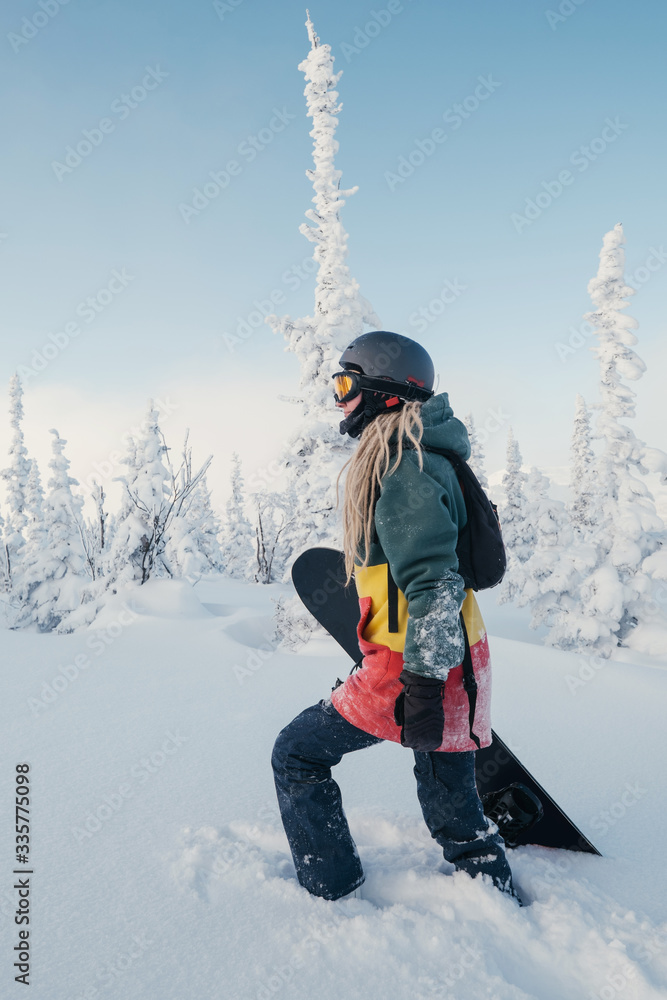 Female snowboarder wearing long dreadlocks and ratsa hoody in white winter forest walking in snow powder