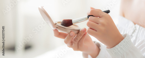 Фотография hand of beauty young asian woman with face looking mirror applying makeup with brush cheek in the bedroom, beautiful girl holding blusher facial, skin care and cosmetic concept, banner website