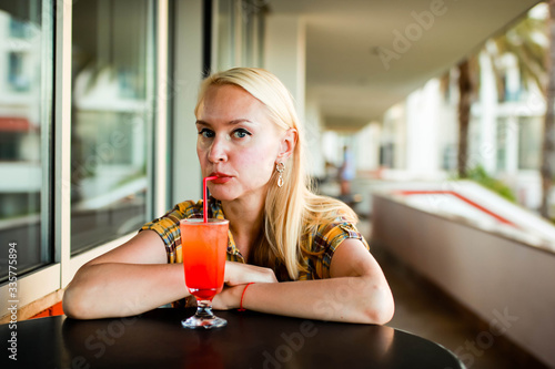 Pensive beautiful young woman in a yellow plaid shirt drinkinng cocktail and thinking. photo