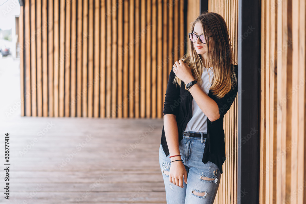 Fototapeta premium Portrait of a young woman on the wooden background with vertical boards. Beautiful girl with long hair and glasses smiling