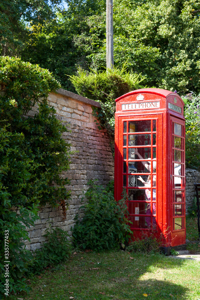 Bibury (England), UK - August 05, 2015: A red phone box in Bibury village, Gloucestershire, England, United Kingdom. Bibury (England), UK - August 05, 2015: A red phone box in Bibury village, Gloucestershire, England, United Kingdom.