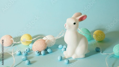 Easter bunny with colorful eggs shaped lights string on pastel color blue background and decor eggs falling down as rain, holiday concept.