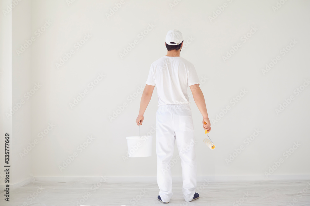 A male painter in a white uniform with a roller works in his hand in a white room A male painter in a white uniform with a roller works in his hand in a white room