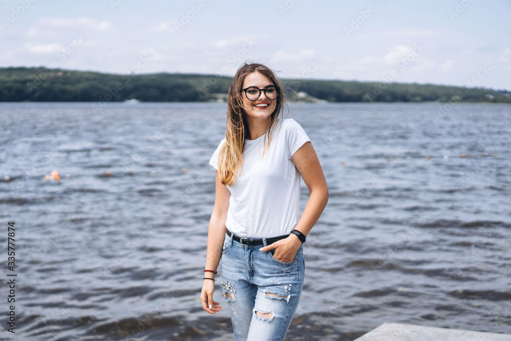 Portrait of a beautiful young woman in stylish glasses. Girl in white tshirt posing on the background of the lake landscape Portrait of a beautiful young woman in stylish glasses. Girl in white tshirt posing on the background of the lake landscape