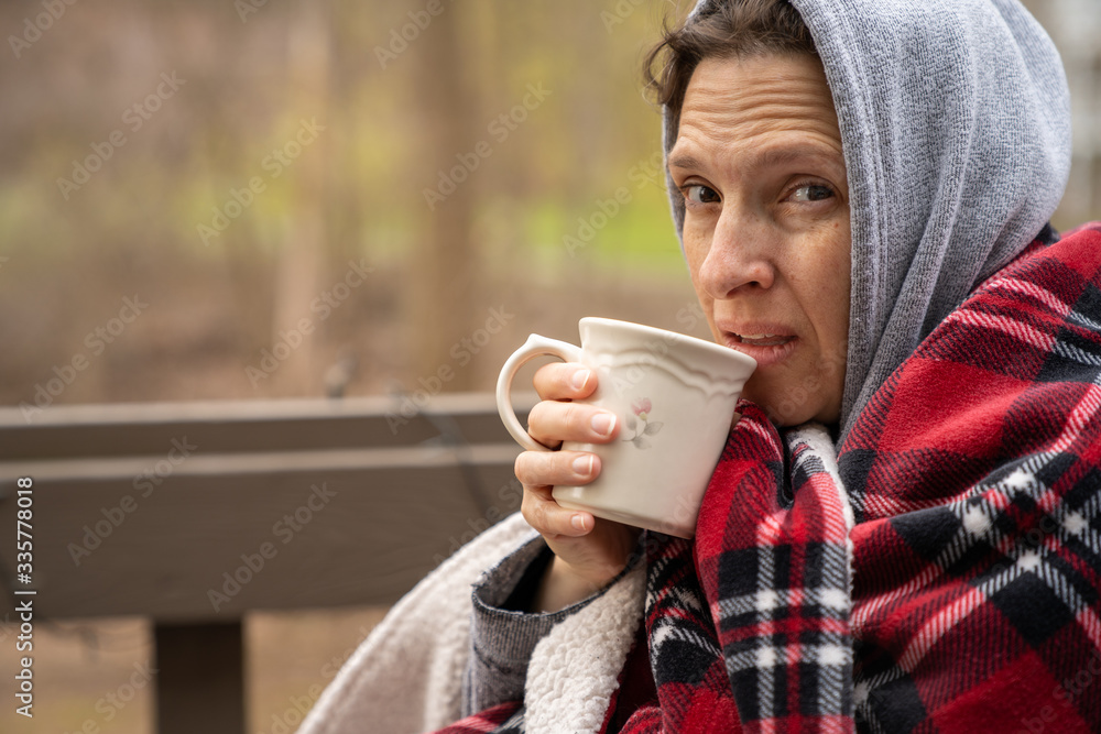 Middle age woman wrapped in a plaid wool blanket with coffee. Middle age woman wrapped in a plaid wool blanket with coffee.