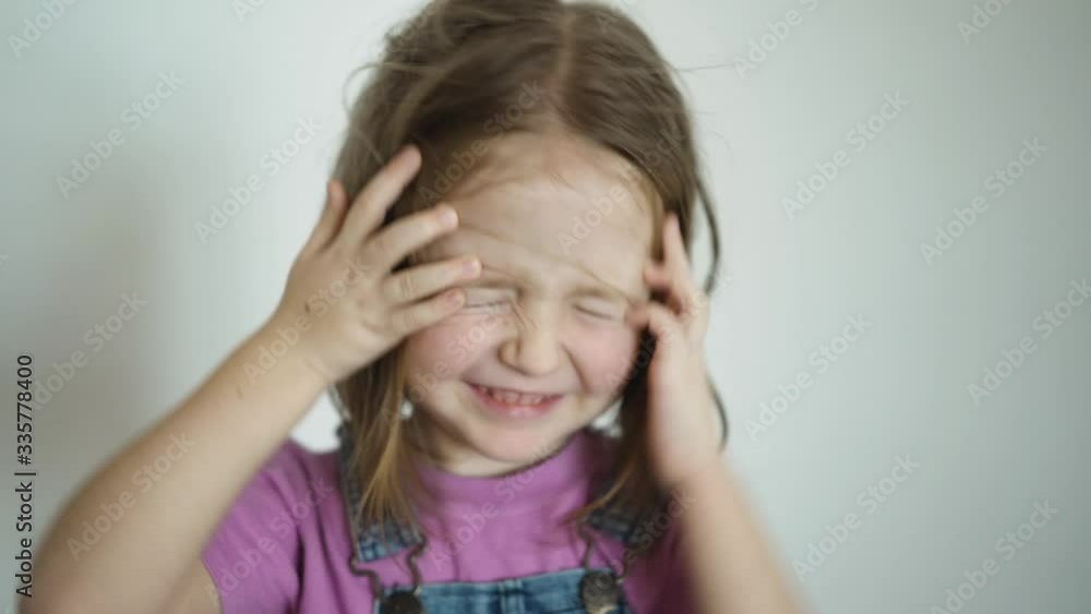 Face of little cute girl when the hair is flying child sweeps away flying hair from face indoor on white background Face of little cute girl when the hair is flying child sweeps away flying hair from face indoor on white background