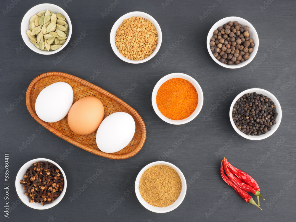 Raw chicken eggs, black pepper, turmeric, masala powder, red chili, cloves, allspice, green cardamom on black wooden background. Ingredients for making scrambled eggs or omelet. Organic food concept Raw chicken eggs, black pepper, turmeric, masala powder, red chili, cloves, allspice, green cardamom on black wooden background. Ingredients for making scrambled eggs or omelet. Organic food concept