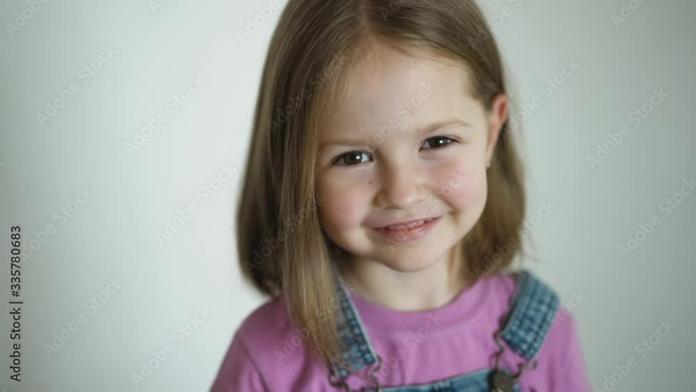 Preschool girl looks at the camera smiling, then resents crossing arms on her chest, close-up of little blonde cute girl’s face. Face portrait closeup. Preschool girl looks at the camera smiling, then resents crossing arms on her chest, close-up of little blonde cute girl’s face. Face portrait closeup.