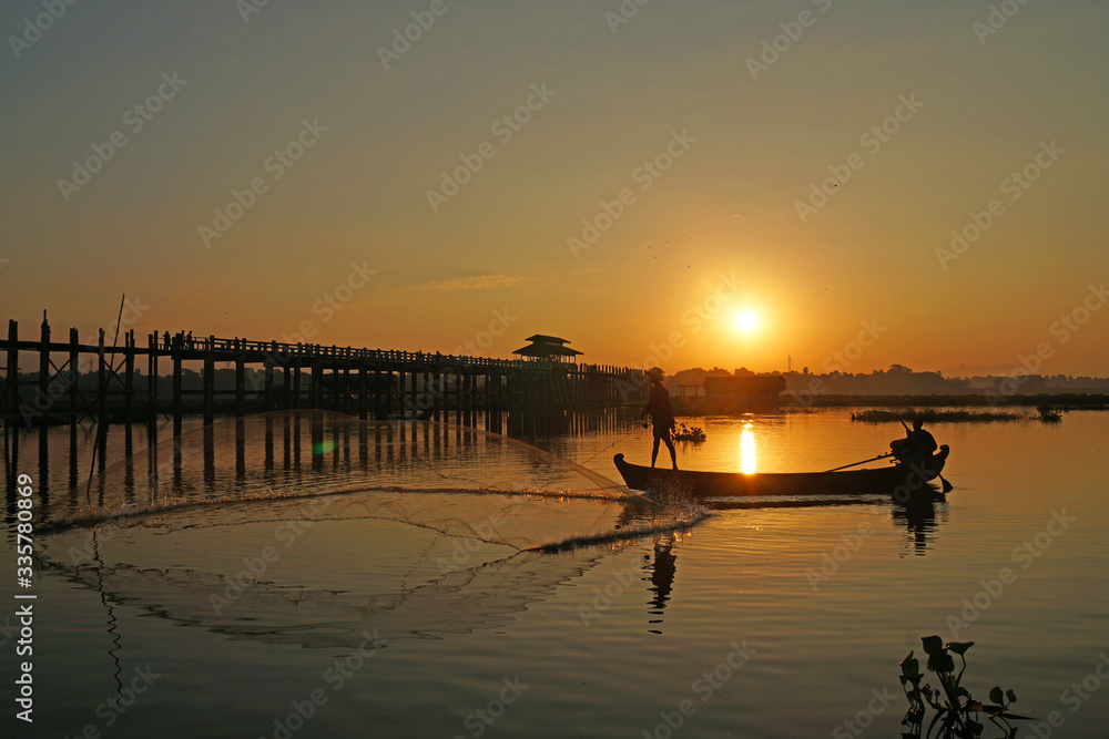 Landscape - nature scene of Silhouette  longest wooden bridge and traditional fisherman boat  on the lake at u bein bridge with sunrise. This place is famous landmark in Mandalay, Burma (Myanmar)