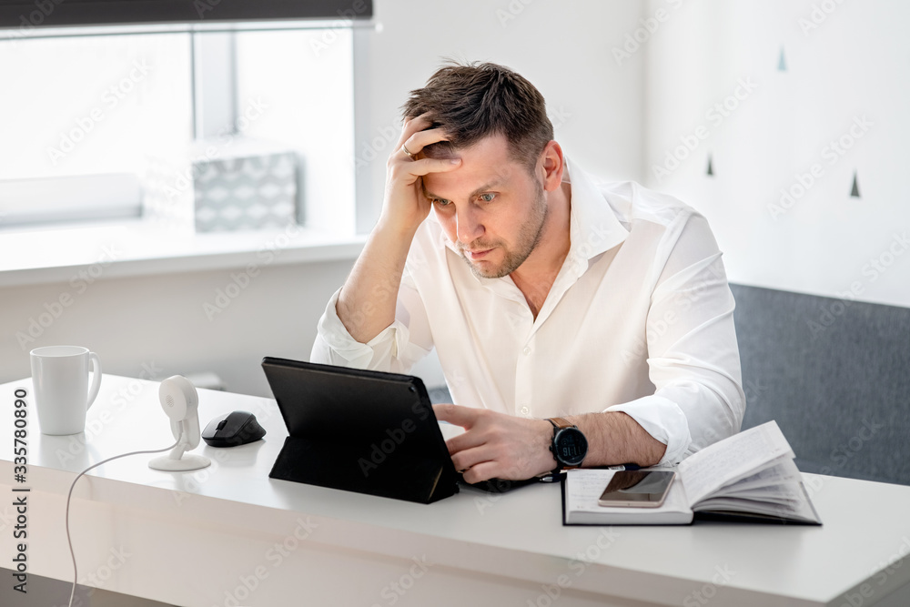 Side view shot of pensive young man sitting at home and working on laptop. Caucasian male working from home office.