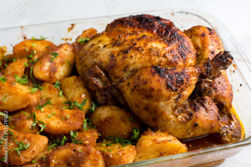 Baked whole chicken with potatoes and herbs in a rustic style. Top view, side view on a light background. Close-up and medium plan. Space for text.