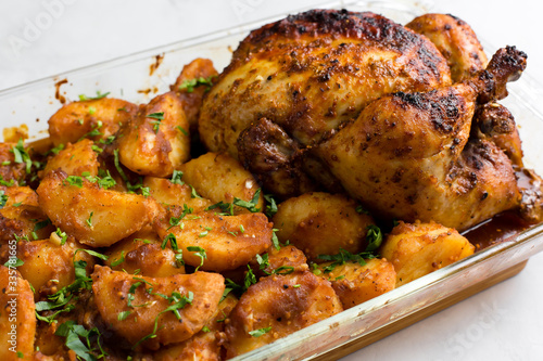Baked whole chicken with potatoes and herbs in a rustic style. Top view, side view on a light background. Close-up and medium plan. Space for text.